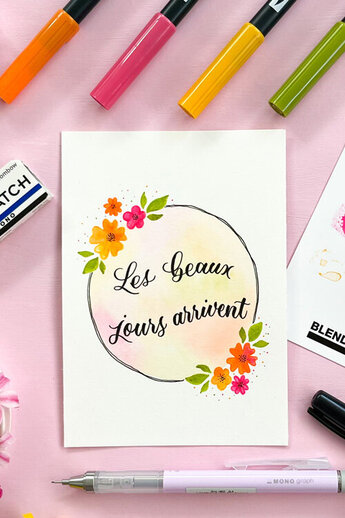 Een lente-achtige illustratie met de inscriptie "Les beaux jours arrivent", omringd door kleurrijke bloemen, potloden en een mengpalet.