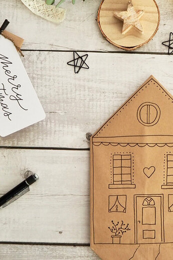 Kerstcadeauzakjes van kraftpapier: links met sterren en "Merry Christmas" label, rechts liefdevol geïllustreerd als een huis. Versieringen en stiften ertussen - perfecte DIY-inspiratie.