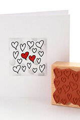 Een wenskaart met een zwart hartjesstempelmotief met enkele hartjes ingekleurd in rood. Daarnaast staat de houten stempel met het hartmotief - perfect voor liefdevolle DIY-kaarten.