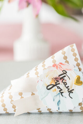 Met liefde gemaakte cadeauverpakking van gedessineerd papier, versierd met lint, een bloemenlabel met "Dank je wel"-letters en een gouden hartsticker. Perfect als klein gastcadeau of tafeldecoratie.