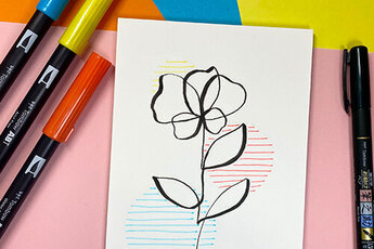 Floral one-line drawing on white card, supplemented with coloured lines in blue, yellow and red, surrounded by coloured markers on a colourful background.